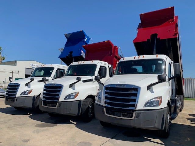 front of three dump trucks